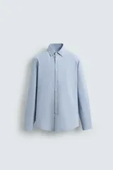 Camisa celeste con finas rayas verticales blancas, de corte regular, cuello italiano, manga larga con puños abotonados y cierre frontal con botones.