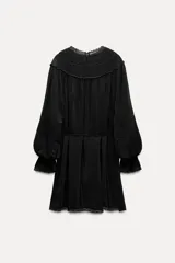 Vestido corto negro con cuello redondo, mangas largas abullonadas con puños elásticos y detalle de encaje y bordados con abalorios. Incluye lazo para ajustar en la cintura.