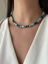Collar corto de cuentas de colores: turquesa, azul marino, verde oscuro, naranja y blanco con manchas negras.