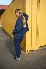 Jean de tiro superalto con pierna amplia y corte holgado. Presenta un diseño de cinco bolsillos, cierre con botón y un doblez ancho en el bajo que deja ver el revés de la tela. Confeccionado en denim con estampado de rayas finas verticales.