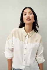 Camisa de lino color crudo y beige, con diseño bicolor y recorte ondulado en el canesú. De silueta relajada, cuenta con mangas amplias y puños camiseros. Se completa con botones de nácar.