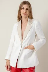 Blazer de lino color blanco con solapas y cuello en color beige, corte entallado, botón de nácar, tajo en la espalda y bolsillos laterales.