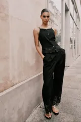 Pantalón culotte negro de tiro alto con pinzas delanteras, bolsillos frontales y falsos bolsillos de vivo en la espalda. Presenta pernera ancha y corta con bordados florales a tono en el ruedo. Cierre frontal con cremallera, botón interior y gancho.