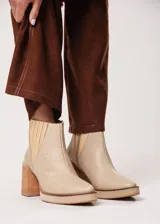 Botín de cuero color beige con textura reptil, elástico lateral y cierre interno. Tiene plataforma delantera y taco de madera.