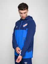 Campera técnica liviana blanca con capucha, cierre frontal y bolsillos laterales. Presenta el logo de Umbro en el pecho izquierdo y el escudo del Club Nacional de Football en el pecho derecho.