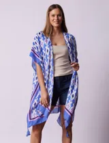 Kimono tejido con estampado abstracto en tonos azules, violetas y blancos. Tiene terminación de ruedo con borlas.