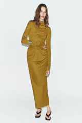 Vestido largo color mostaza con cuello alto, manga larga drapeada y detalles cut out laterales. Presenta frunces en la cintura y la espalda, y bajo recto.