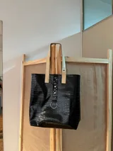 Bolso tote negro con textura símil cuero de cocodrilo, con bolsillo frontal marrón y herrajes plateados.