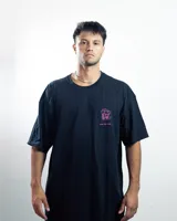 Remera negra de algodón con cuello redondo y mangas cortas. Presenta un estampado pequeño en el pecho con un diseño abstracto en tonos rosa y celeste.