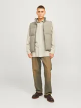 Chaleco acolchado sin mangas color gris topo, con cuello alto y cierre de cremallera. Tiene bolsillos frontales y relleno de fibra sintética.