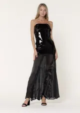 Vestido largo de fiesta strapless, con cuerpo superior de lentejuelas negras y falda de gasa plisada con godets. El diseño combina texturas contrastantes para crear movimiento y sofisticación.