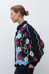 Camisa de manga larga, color azul marino, con estampado floral en tonos rojo, blanco y celeste. Presenta un diseño frontal con paneles ondulados en color celeste claro.