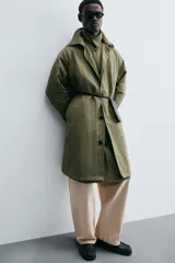 Trench color verde oliva de tejido técnico, corte relaxed fit, cuello solapa, manga larga, bolsillos laterales y abertura en la espalda.