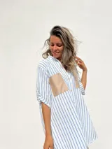 Camisola a rayas verticales azules y blancas, con cuello en V, mangas 3/4 y dos bolsillos cuadrados de gamuza color beige en el pecho.