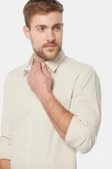Camisa de lino color beige, de manga larga, con cuello clásico y bolsillo en el pecho.