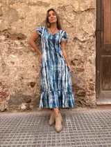 Vestido largo con estampado tie-dye en tonos azules y blancos, con mangas cortas con volados y falda con volados en el ruedo.