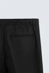 Pantalón negro de corte regular fit, confeccionado en tejido de lino. Presenta cintura con botón y cierre de cremallera, bolsillos frontales y bolsillos traseros de doble vivo.