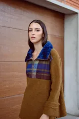 Buzo marrón de lana con mangas rectas, largo medio y cuello con cierre. Aplique de corderito azul en el cuello. Buzo amplio con diseño a cuadros en la parte superior.