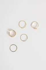 Set de cinco anillos dorados de diferentes diseños: uno liso, uno con textura y una pequeña circonita, uno con una estrella, uno con una flor y uno con diseño geométrico de triángulos.