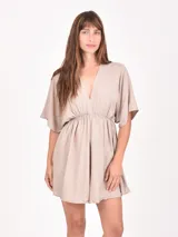 Monoprenda corta color beige claro con escote en V profundo, mangas cortas tipo mariposa y cintura fruncida elástica.