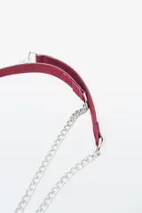 Cartera de mano o clutch color rojo oscuro (bordó) con textura de gamuza o terciopelo. Presenta tachas metálicas plateadas a lo largo del borde inferior y lateral, y un cierre perimetral plateado. Incluye una correa de hombro desmontable compuesta por una tira de material a tono y cadena metálica plateada.