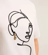 Remera blanca de algodón con cuello redondo y bordado de una cara de mujer con caravana dorada.