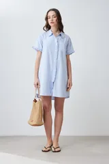 Vestido camisero corto de color fucsia, con detalles de volados en el cuello, los puños de las mangas cortas y a lo largo de la cartera de botones frontal. Presenta un diseño de silueta holgada y corte recto.