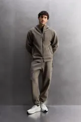 Pantalón jogger color marrón oscuro, corte regular fit, confeccionado en tejido técnico compacto de algodón con elasticidad. Cuenta con cintura elástica ajustable con cordón, bolsillos frontales y bolsillo lateral con cierre de cremallera.