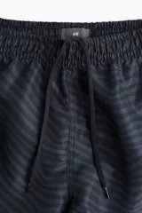Short de baño negro con estampado de líneas onduladas en tono más oscuro. Cuenta con cintura elástica, cordón de ajuste interno, bolsillos laterales y suspensor interno de malla.