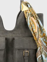 Cartera de hombro de ecocuero color gris, con compartimento principal con cierre cremallera, dos bolsillos frontales con solapa y broche imantado, bolsillo interior con cierre y bolsillo trasero con cierre. Incluye un pañuelo estampado como adorno.
