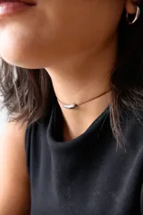 Gargantilla con tiento de hilo encerado color borgoña y dije de acero quirúrgico hipoalergénico plateado en forma de tubo.