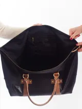 Bolso negro con detalles en cuero marrón, con doble asa de mano y cierre superior.