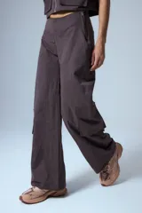 Pantalón cargo marrón de gabardina, con cierre metálico lateral, elástico en cintura trasera, recortes delanteros y bolsillos tipo cargo.