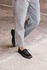 Mocasín de cuero negro con cordones y tachas metálicas en la puntera.