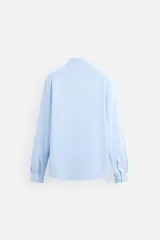 Camisa celeste a rayas verticales blancas, de corte recto, con cuello italiano abierto, manga larga con puños abotonados y cierre frontal con botones.