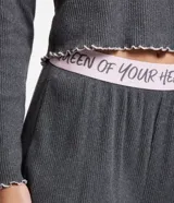 Conjunto de pijama largo gris de punto, compuesto por una blusa de mangas largas con cuello redondo y un bordado de corazón en el centro, y un pantalón con cintura elástica y lettering "Queen of your heart".