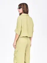 Camisa negra de manga corta con cuello camisero y botones frontales. Presenta un corte cropped y textura acanalada o plisada.