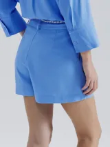 Short de lino blanco, de corte recto y tiro alto, con trabillas para cinturón y un lazo trenzado de color crudo anudado en el frente.