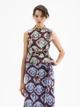 Top sin mangas de viscosa, con escote redondo y volado en el ruedo. Presenta un estampado full print con motivos florales y figuras humanas estilizadas en tonos borgoña, verde menta y amarillo.