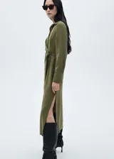 Vestido camisero midi color verde oliva, con cuello camisero, mangas largas con puños abotonados, cierre frontal con botones, cinturón con hebilla forrada y abertura lateral en el bajo.