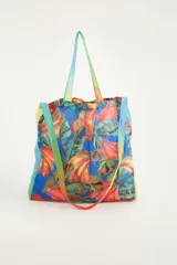 Bolso tote de poliéster con estampado de bananas y hojas en tonos naranja, verde y amarillo sobre fondo azul. Asas de hombro con degradé de colores.
