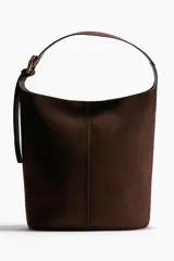 Bolso tipo bombonera de color marrón oscuro, con textura de gamuza o nobuck. Posee un asa de hombro ancha y ajustable con hebilla metálica dorada.