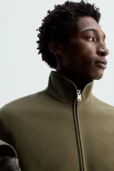 Sobrecamisa verde militar de tejido polar, corte regular fit, cuello alto, manga larga, bolsillos laterales y cierre frontal con cremallera.