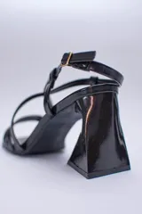 Sandalias de tacón alto color violeta metalizado, con tiras finas cruzadas en el empeine, puntera cuadrada y cierre con hebilla en el tobillo. El tacón es geométrico con forma de triángulo invertido.