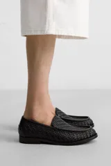 Mocasín de cuero negro con diseño trenzado en la parte superior, horma redonda y suela con ligero tacón.
