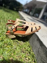 Sandalias nude de cuero con diseño calado y tira con hebilla al tobillo.