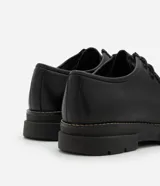 Zapato de vestir negro con cordones, fabricado en cuero sintético, con puntera redondeada y suela de goma.
