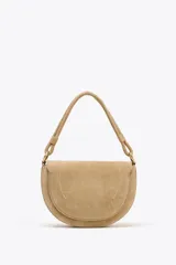 Bolso bandolera de gamuza color beige, con asa corta y correa larga extraíble. Cierre con solapa imantada y bolsillo interno con cierre.