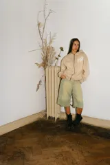 Hoodie con cierre frontal de algodón color crema con lavado acid wash. Presenta un logo estilizado en el pecho y estampados gráficos con caracteres orientales en ambas mangas.