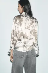 Camisa de manga larga con cuello solapa y estampado abstracto en tonos marrones y blancos. Cierre frontal con botones y bajo asimétrico.
